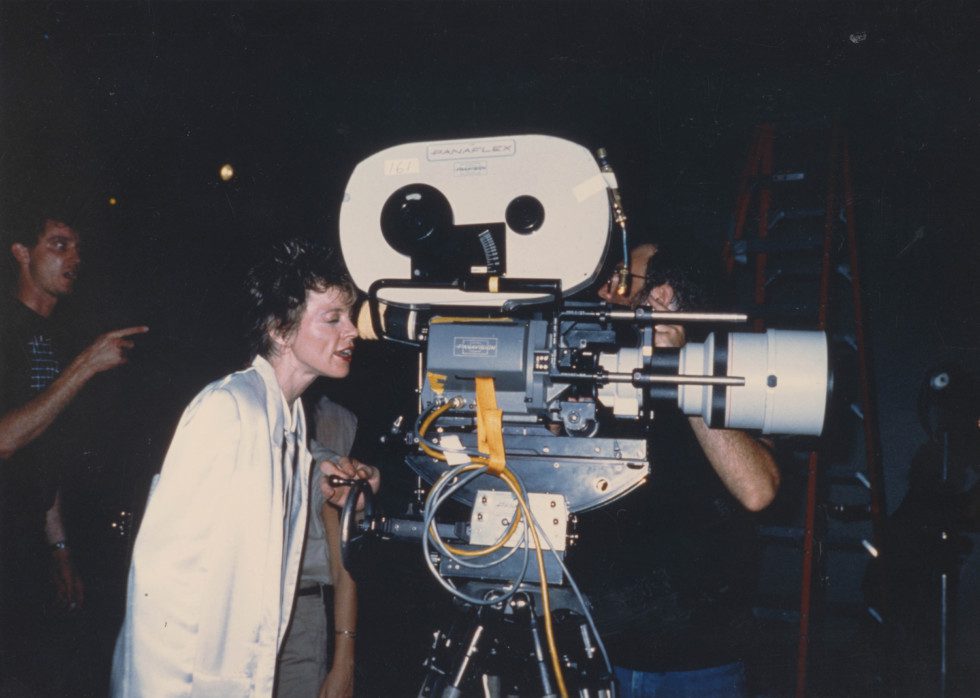 En person (Laurie Anderson) står lutad mot en stor filmkamera