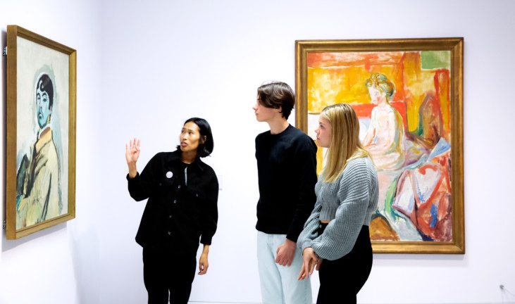 Tre personer som står och tittar på målningen "Självporträtt" av Harald Giersing. Bakom dem syns Edward Munchs "Pike paa sengekant"