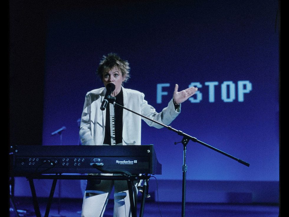 from Home of the Brave. Laurie Anderson behind a keyboard against a blue background