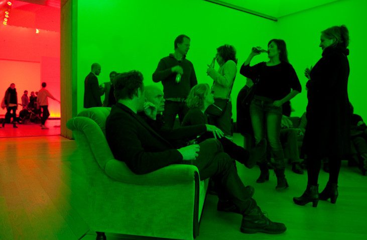 People in a room lighted with green lights, talking and mingling