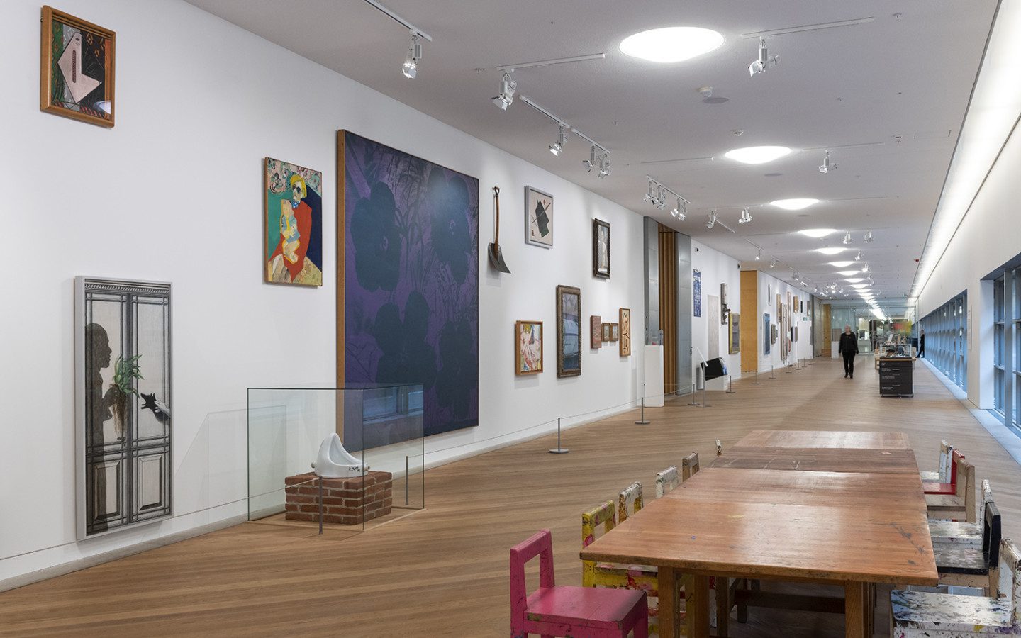 Photo of an oblong white room with wooden floors. On the walls hang works of art in different colors, sizes and styles.