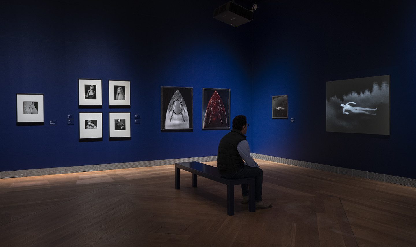 A man is sitting on a bench, looking at art works in the exhibition "Sleepless Nights"