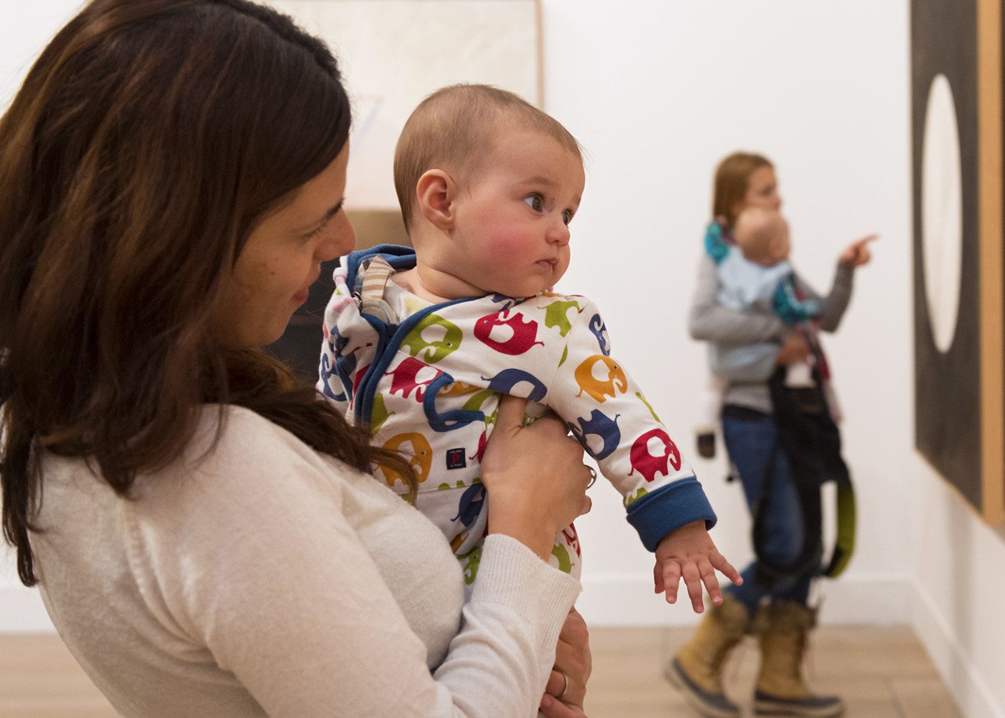 A baby dressed in pyjamas looks at a painting