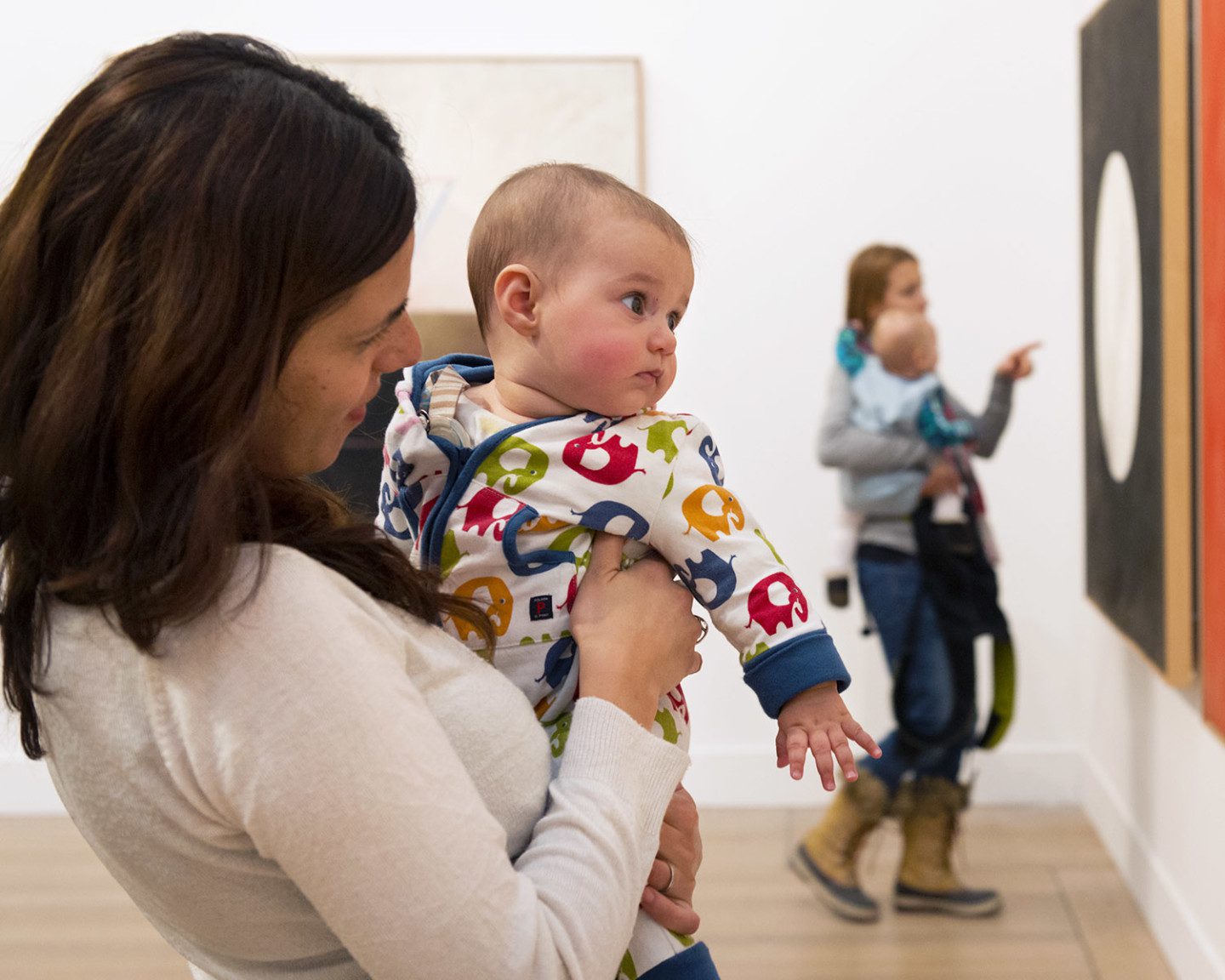 A baby dressed in pyjamas looks at a painting