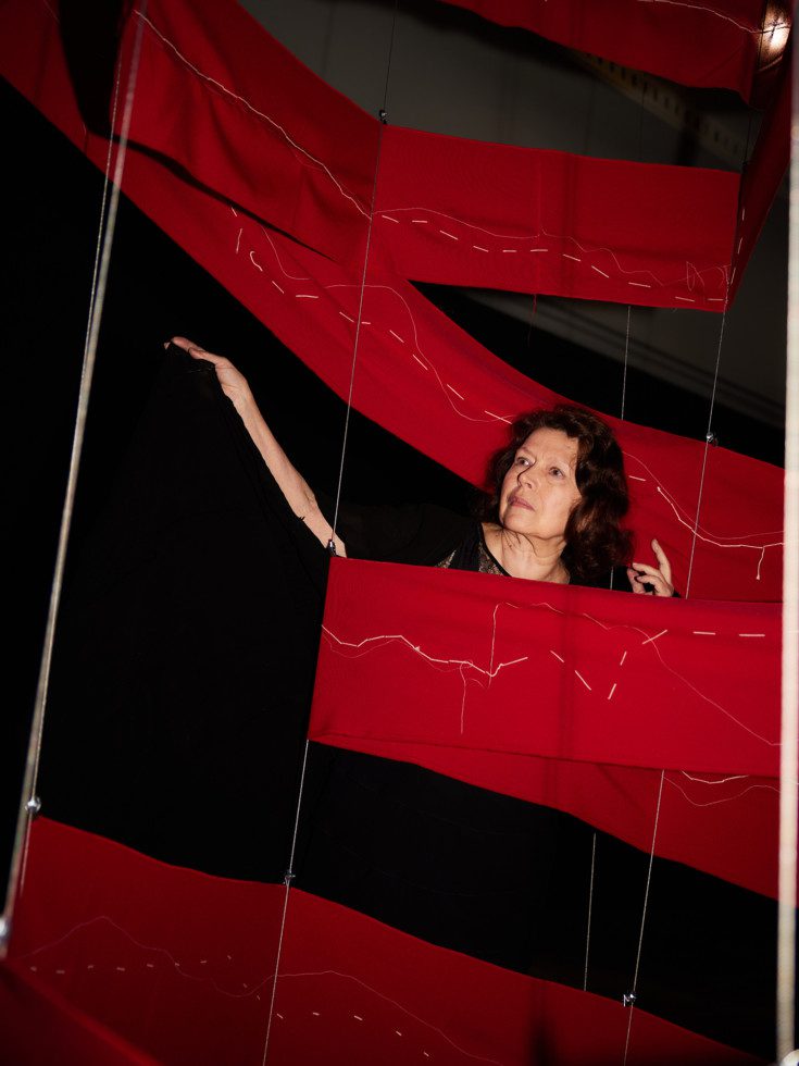 Photograph Katalin Ladik, in the middle of a red draped fabric, bakgrunden är svart