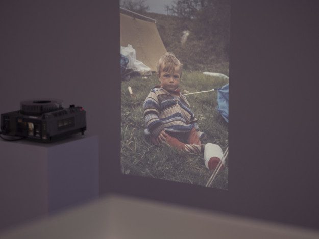 Diapositive of a child in a striped shirt, sitting in grass.