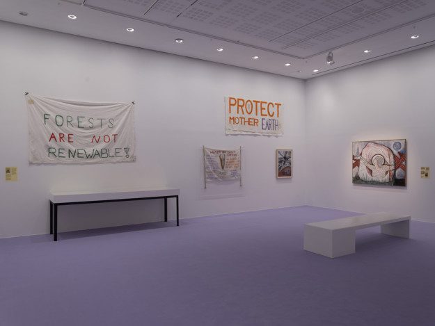 Installation view over the exhibition. Artworks and protest banners are displayed on the walls. The room has purple walls and a purple carpet.