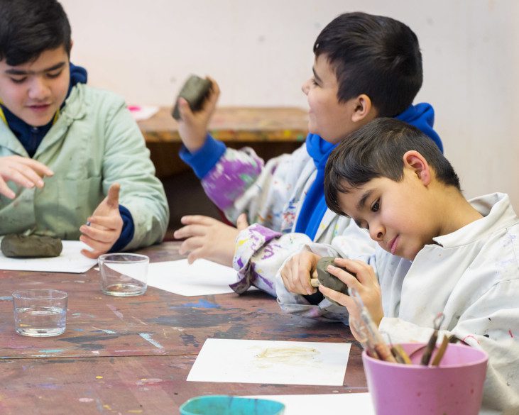 Three children creating with clay by a wooden table