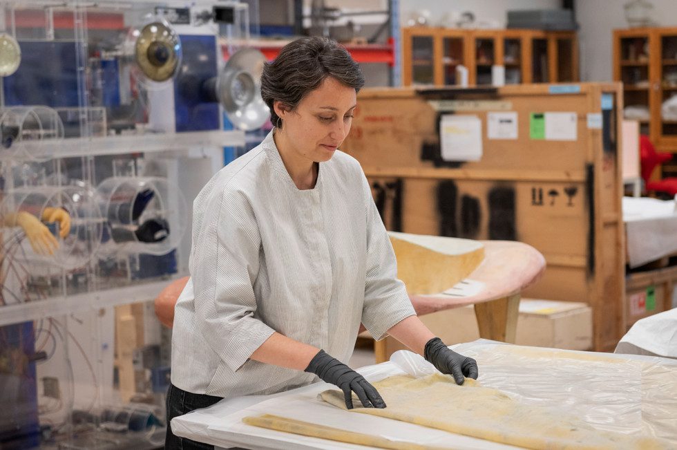 Conservator Michaela Florescu standing in the conservation department, handleing an artwork