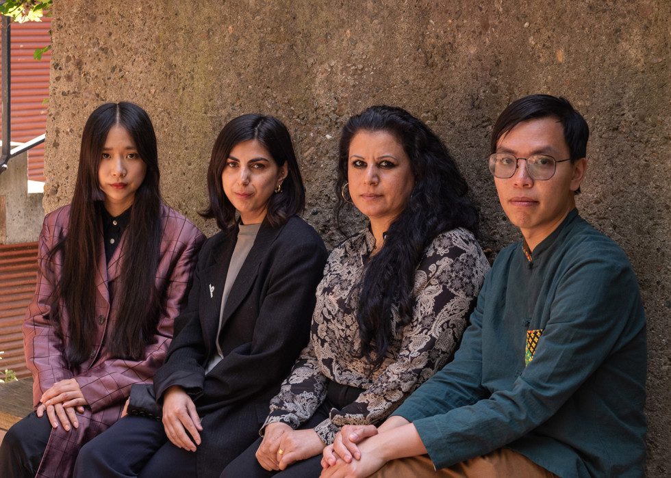 Photo of four persons sitting on a bench against a gray concrete wall