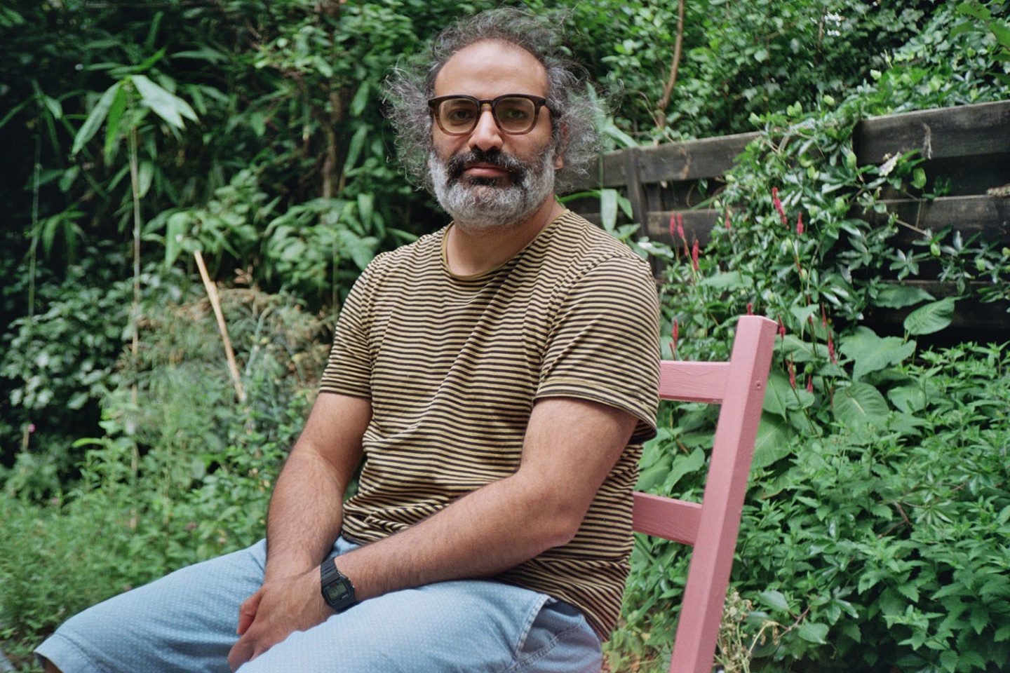  Foto av Yazan Khalili, sittande på en trästol med vegetation i bakgrunden