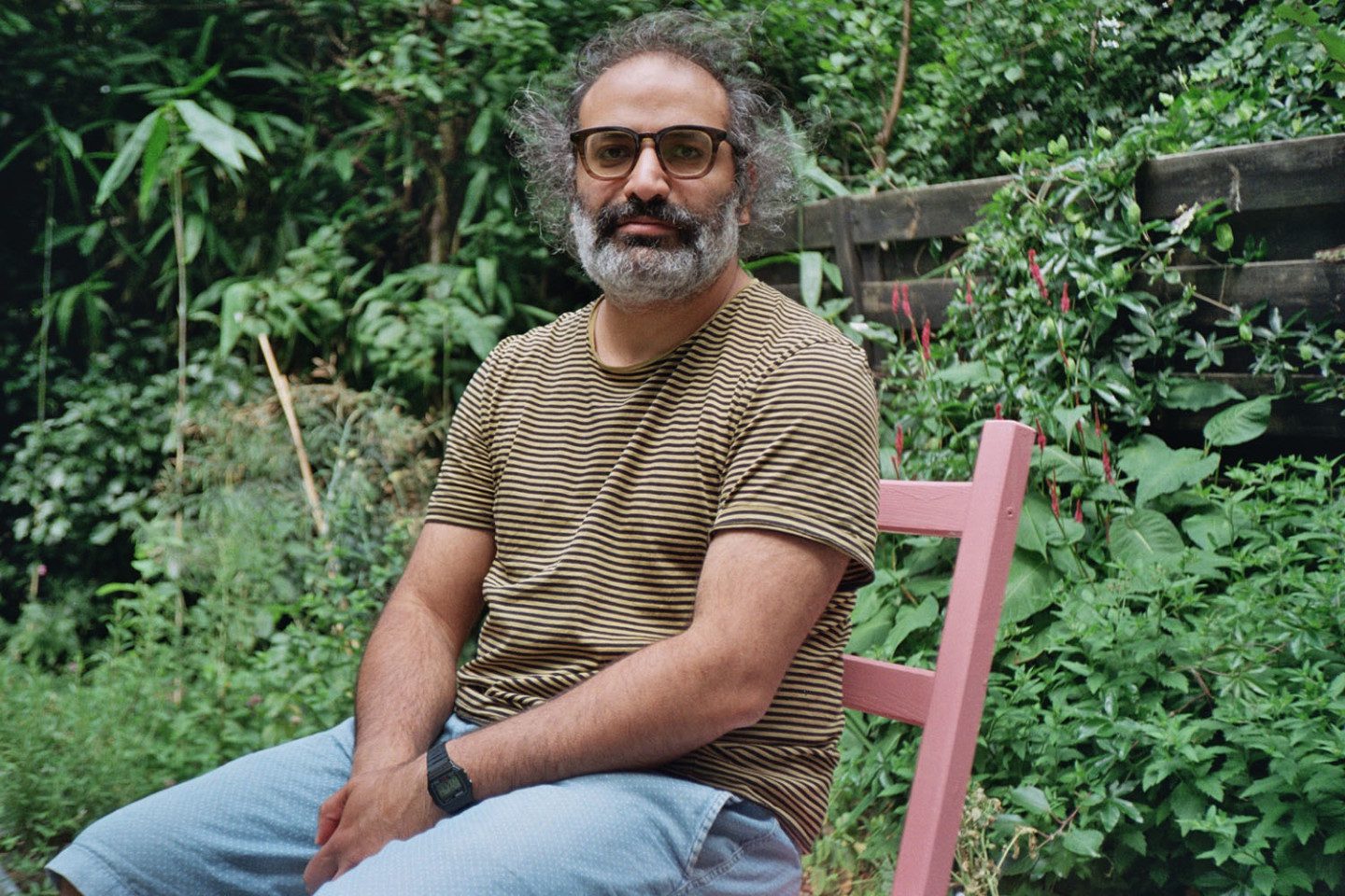 Photo of Yazan Khalili, sitting on a wooden chair with vegetation in the background