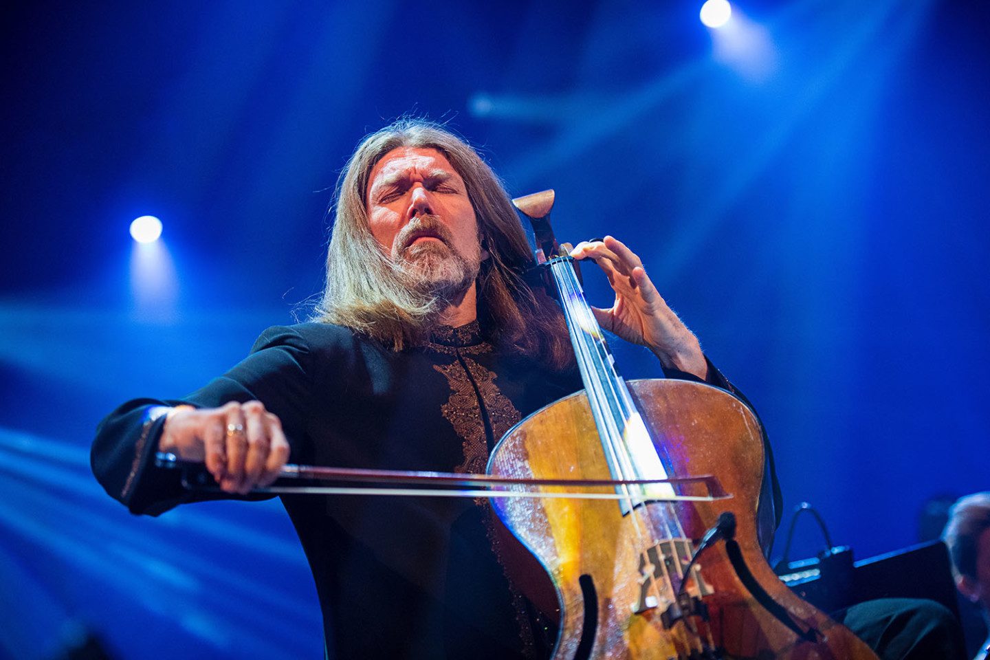 Musikern Svante Henryson spelar cello under en konsert, blå bakgrund