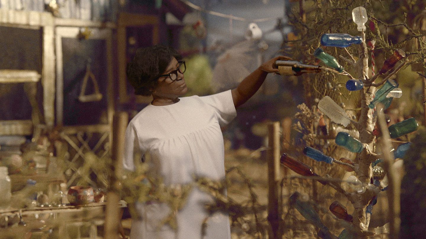 A doll-looking person is watering a tree with a flask made out of glass. The tree has flasks instead of branches. 