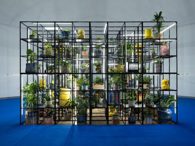 An iron grid filled with plants, lights and pottery