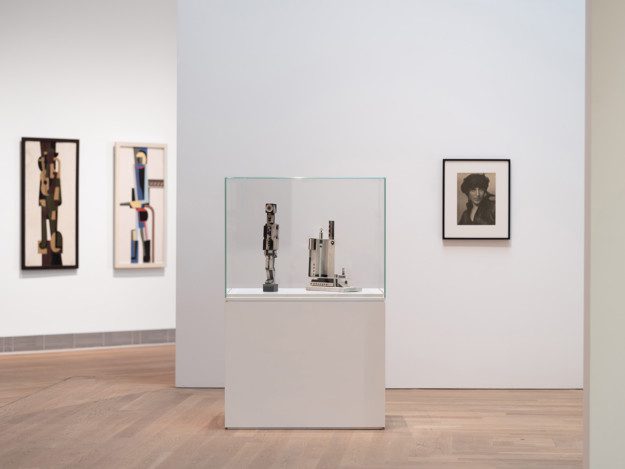 Bild av ett rum med vita väggar med tavlor hängda på. Ett podium finns i mitten av bilden med två skulpturer i.