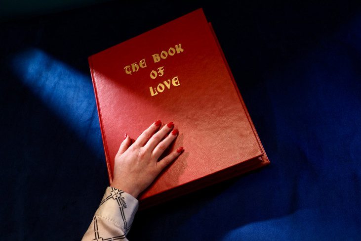Film still from Bodily Remains, a hand is placed on a book, the title of the book is "the book of love"