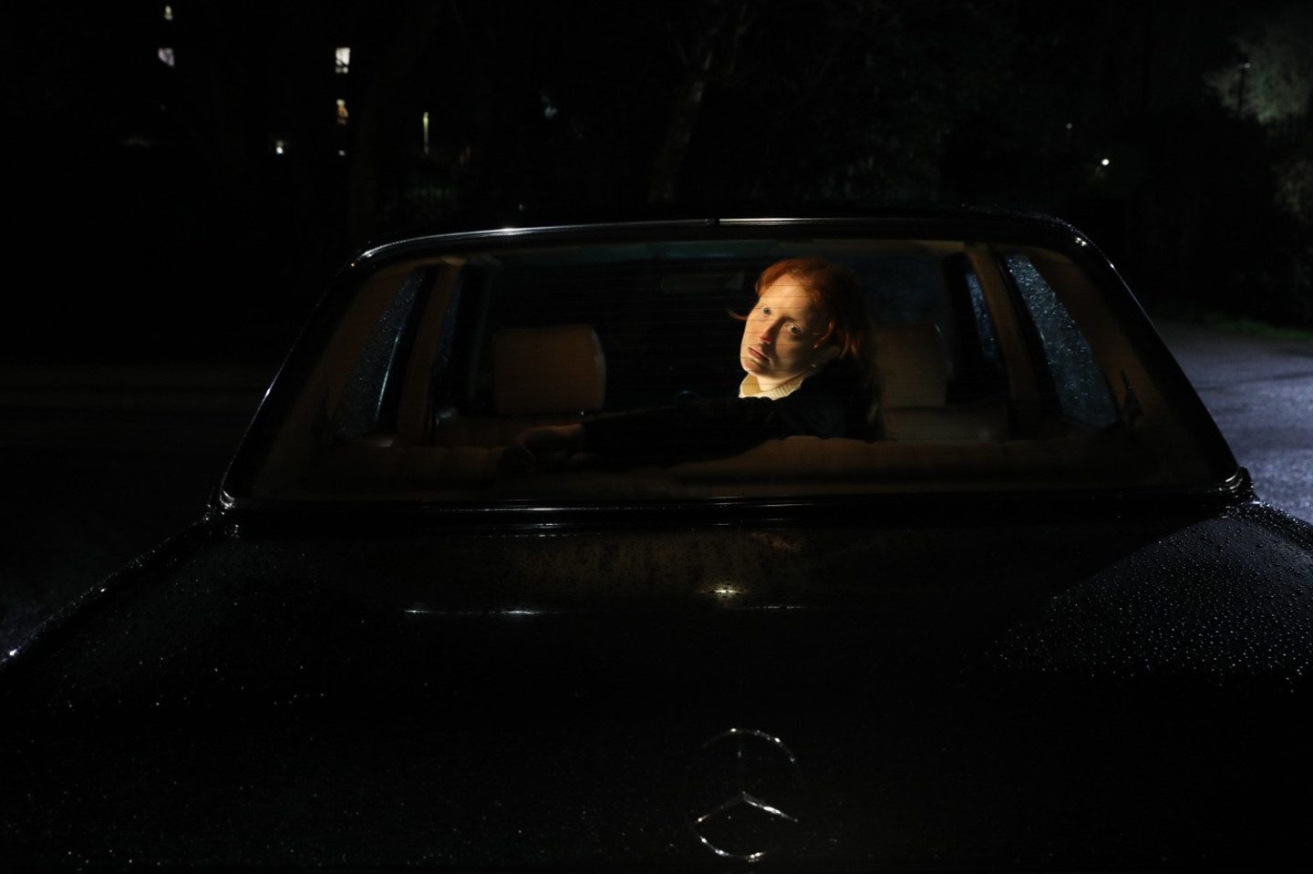 Film still from Bodily Remains, a person looking back thorugh a car window
