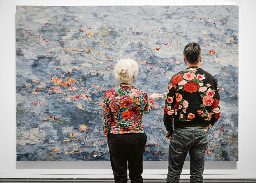 Two people in floral tops in front of a large artwork with flowers