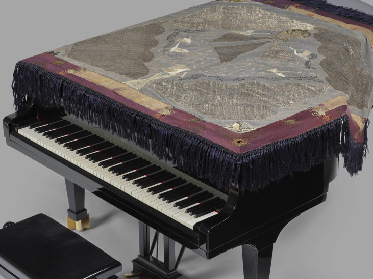 Svart piano med broderat flygeltäcke i färg